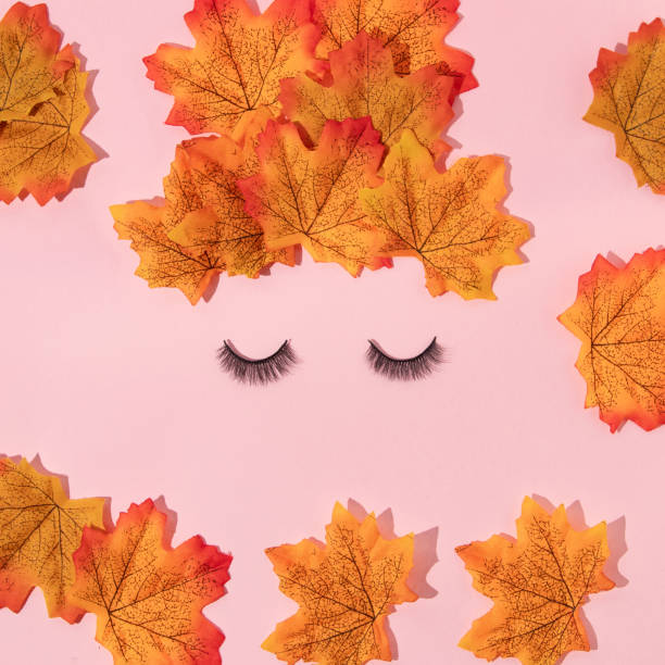 Autumn creative layout made with leaves and false eyelashes on pastel baby pink background. Vintage retro aesthetic 80s or 90s fashion concept. Minimal autumn season idea.
