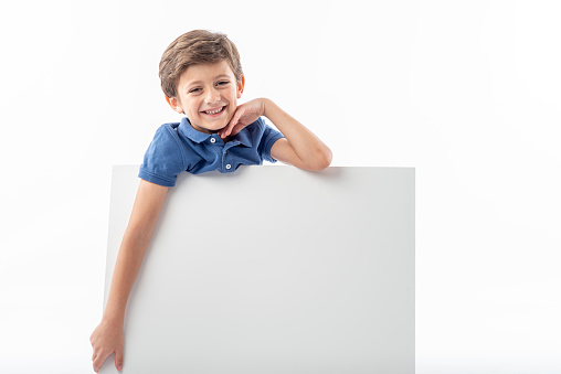 Smiling Caucasian boy showing a white advertising poster with space for text, on a white background.