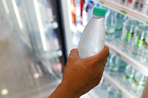 Cropped shot of a man buying a cold bottled water, taking from a fridge in a grocery store