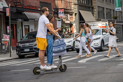 Broadway, Manhattan, New York, NY, USA - July 16th 2022: Young couple with shopping bags on a electric push scooter in front of a zebra crossing