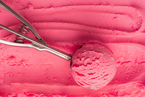 High angle view of scoop of pink cold sweet ice cream or sorbet made with juicy red berries, raspberry or strawberry in metal silver serving spoon on textured gelato background. Refreshing natural dessert