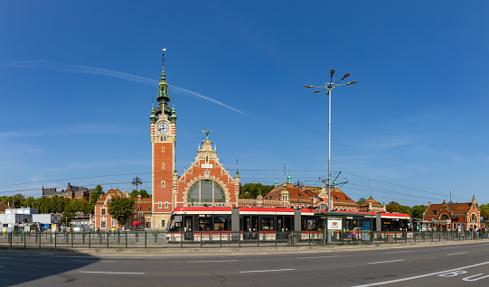 Gdansk, Poland - August 15, 2022: A picture of the Gdansk Main Train Station as seen through the other side of the avenue, with a tram stopped in the center.