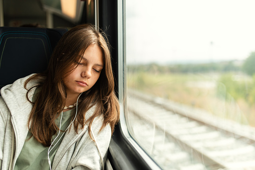 Girl is traveling by train and sleeping while leaning on window. She has headphones in her ears and listening music