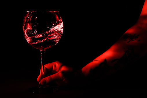 hand holds a glass of water in motion. Black background. red backlight.