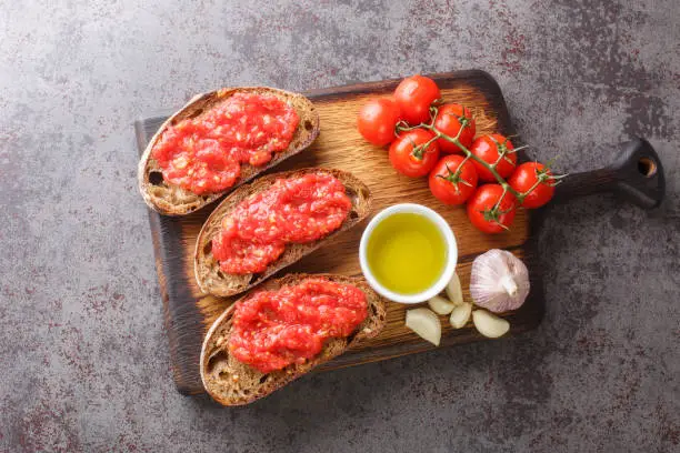 Spanish tomato toast pan tomaca or tostadas con tomate closeup on the wooden board on the table. Horizontal top view from above