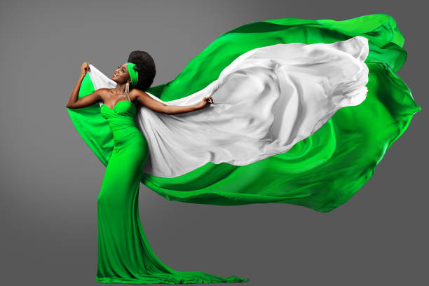 Woman dancing with Nigerian Flag in Green White Dress. Fashion Model with Afro Hair in Long Gown with flying Silk Scarf. Waving Chiffon Fabric over Gray. Nigeria Independence Day stock photo