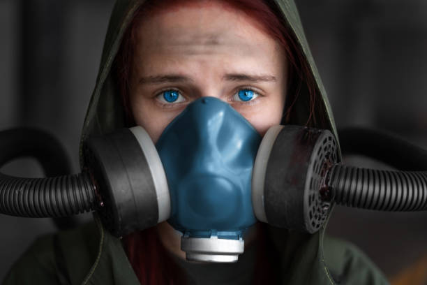 postapokalypse weibliche überlebende. junge pandemie-überlebensfrau in gasmaske, die vor ihr auf den hintergrund schaut, mit apokalyptischen kriegsgebieten. traurige frau in atmender oxy-maske - zeitdieb fotos stock-fotos und bilder