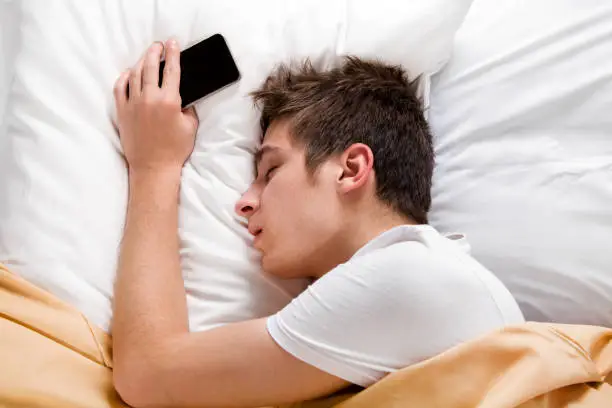Tired Young Man sleep in the Bed with a Mobile Phone