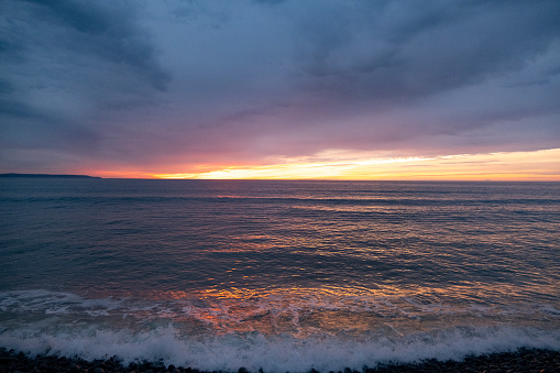 A waves washes up on the shore with a backdrop of a setting sun, North Devon, UK