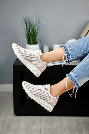 Young woman in blue jeans trying on beige sport shoes in shop, copy space. Woman wearing comfortable stylish sneakers indoors, closeup