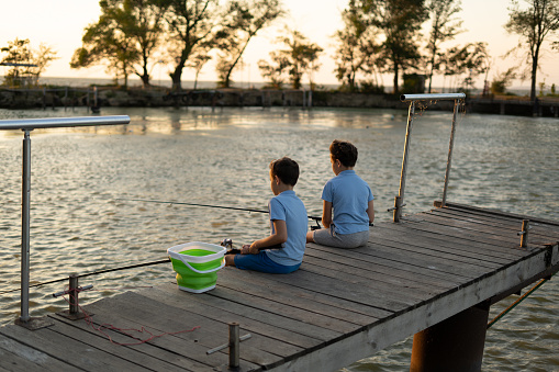 A silhouette of two young boys fishing off a dock.