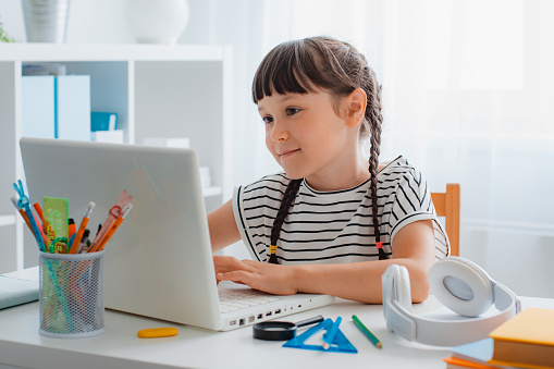 child smile of schoolchildren is a girl at home with a computer studying online, video call education. homework, back to school.