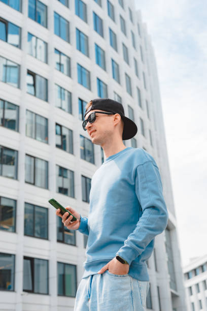 istock Positive hipster guy with backpack standing outdoor holding smartphone while looking away with smile 1424596804