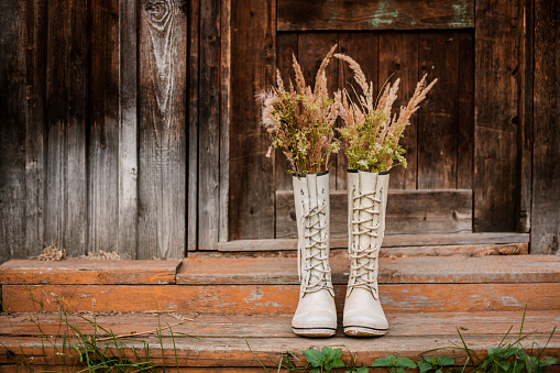 autumn bouquet in rubber boots on the background of old wooden doors and the village threshold. Free space for text. Autumn background.