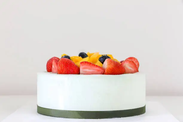 Photo of Sweet fruity birthday cake with fresh strawberries, blueberries and mango, in the middle of a white table