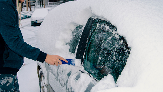 Unrecognizable Man cleaning car window glass from snow on parking. Close up male hand removing snow from the  car