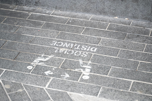 Close up of social distancing graphic sign painted on brick sidewalk