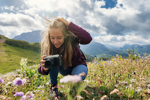Teenage girl hiking in the beautiful high mountains - Alps, Tyrol, Austria. The girl is taking photos of the beautiful flowers in the mountain meadow.\nCanon R5
