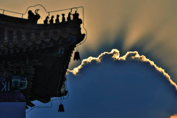 The sun penetrates the dark clouds, in the glow of the rays, silhouettes of ancient buildings in Asia