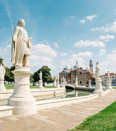 Padua, Italy - September 6, 2022: statues and canal in Prato della Valle square, in the background the basilica of Santa Giustina