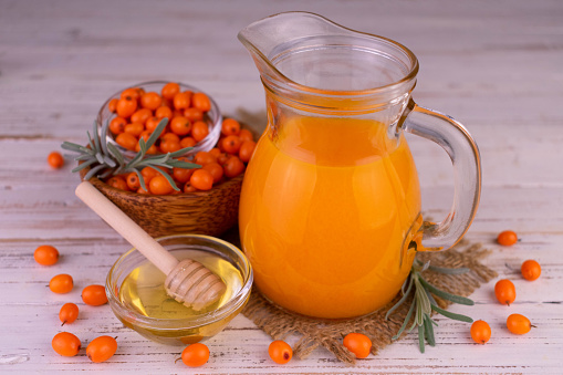 Vitamin sea buckthorn juice with honey in a decanter on a white wooden background.