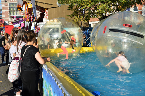 Leuven, Flemish-Brabant, Belgium - September 11, 2022: young girls caucasian girls moving, walking, running and having fun in an aqua bubble water ball on a fun fair attraction in an outdoor water pool