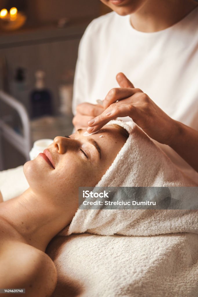 Beautician applying facial cream all over young woman's forehead at spa salon. Skin treatment. Girl facial treatment. Medical health. Facial Mask - Beauty Product Stock Photo