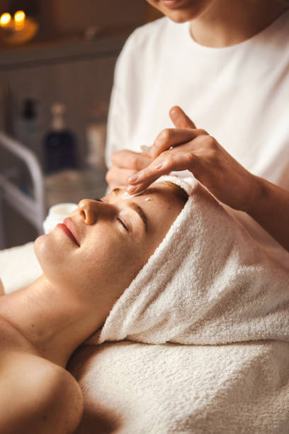 esteticista aplicando creme facial na testa da jovem no salão de spa. tratamento de pele. tratamento facial feminino. saúde médica. - spa - fotografias e filmes do acervo