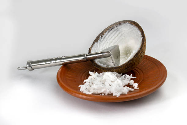 Grated coconut in a mud plate with a coconut hand grater on white background.