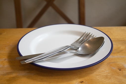Empty white blue rimmed dinner plate on wooden table with cutlery set, front view.