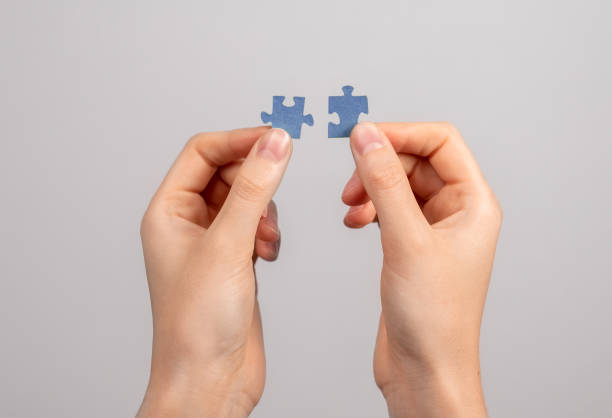 Hands connecting matching jigsaw puzzle pieces. Two details representing companies merging, joint venture, partnership, solution finding.