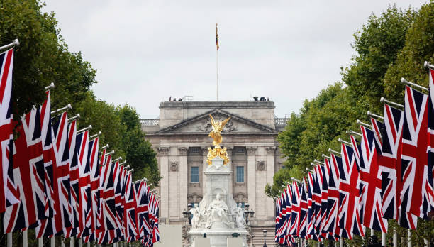 ein blick auf den buckingham palace mit union jack-flaggen, die die mall in london, großbritannien, säumen. - the british red ensign stock-fotos und bilder