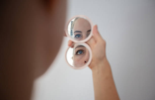 istock Blonde young woman looking at face in hand mirror. 1424643078