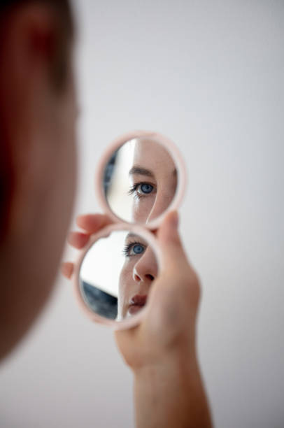 istock Blonde young woman looking at face in hand mirror. 1424643142
