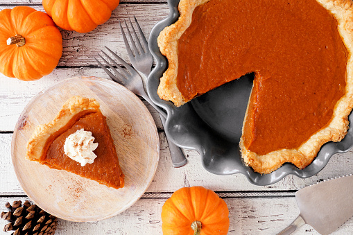 Slice of pumpkin pie with whipped cream topping. Top view table scene on a white wood background.