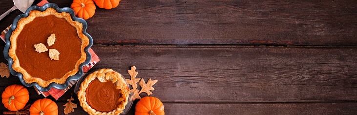 Homemade autumn pumpkin pies. Top down view table scene on a dark rustic wood banner background with copy space.