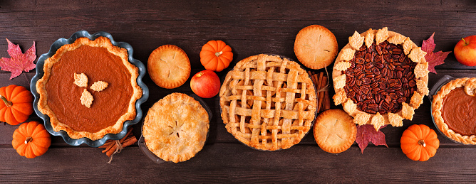 Assorted homemade fall pies. Pumpkin, apple and pecan. Top view table scene on a dark wood banner background.