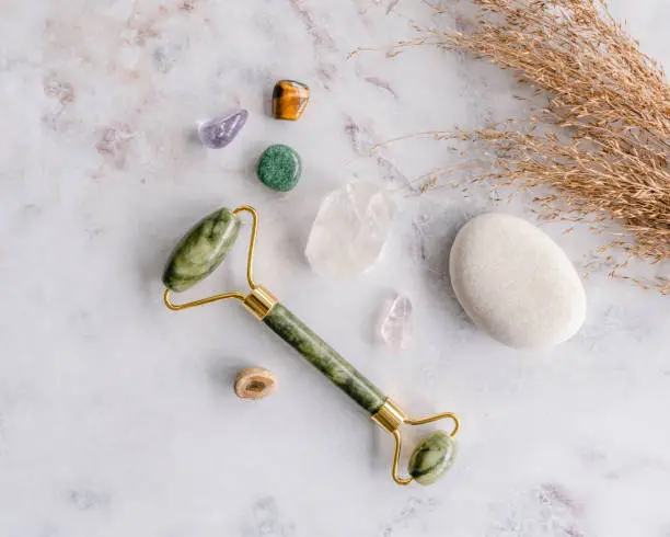 Overhead view of a green face roller on a marble surface next to small stones and crystals