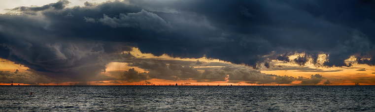 Stormy sea under dark stormy sky with fata morgana on the horizon. Large panoramic seascape at sunset