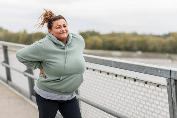 istock Fat Hispanic woman having back pain while exercising by the river 1424650576