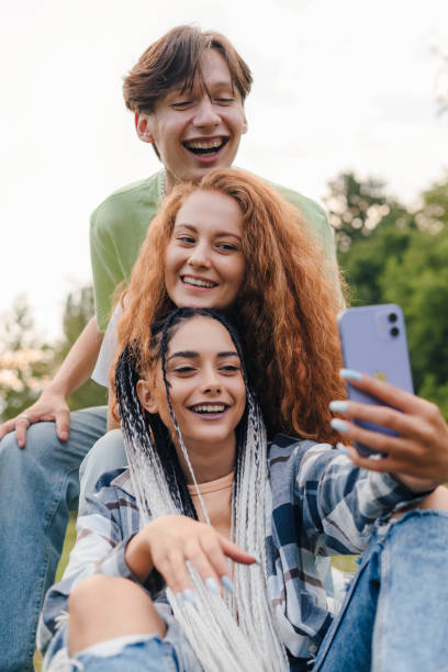 A group of young smiling hipster friends taking selfie self-portrait in park, students having fun and take photo for blog. New technology and blogging concept. stock photo