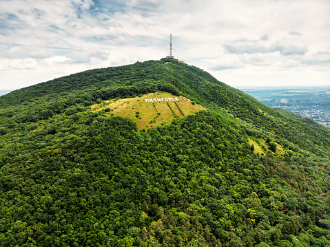 Mashuk Mount in Pyatigorsk, Stavropol Krai, Russia. Landscape of wooded mountain with inscription Pyatigorsk on slope. Scenery of city landmark in summer. Theme of nature, hike, tourism and travel.