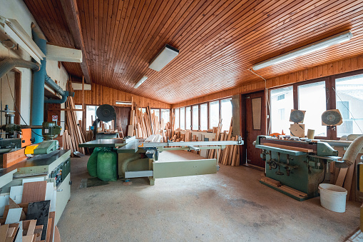 Spacious workshop of a carpenter with wooden ceiling and multiple windows. Room without people used to store material needed for building.