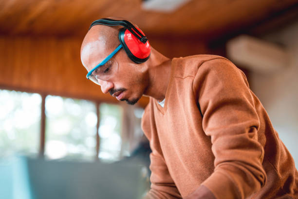 Side portrait of hispanic carpenter. Close up shot of hard working man using protective eyeglasses and canceling noise headphones.