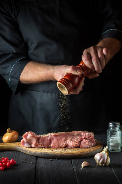 le chef prépare de la viande de veau crue. avant la cuisson, le chef ajoute du poivre au bœuf. un plat national est préparé dans la cuisine du restaurant. - veal calf meat baking photos et images de collection