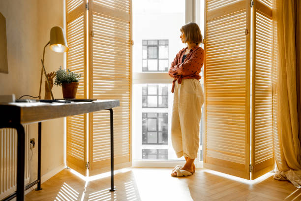 istock Woman stands alone by the window blinds at home 1424661721