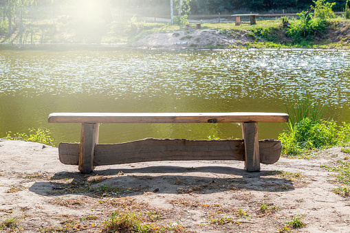 A wooden bench near a pond at daytime.Beautiful view of the lake.The concept of outdoor recreation.sunny. Toned