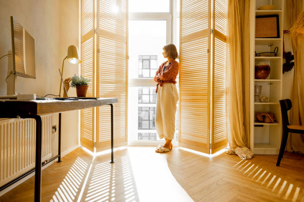 istock Woman stands alone by the window blinds at home 1424665936