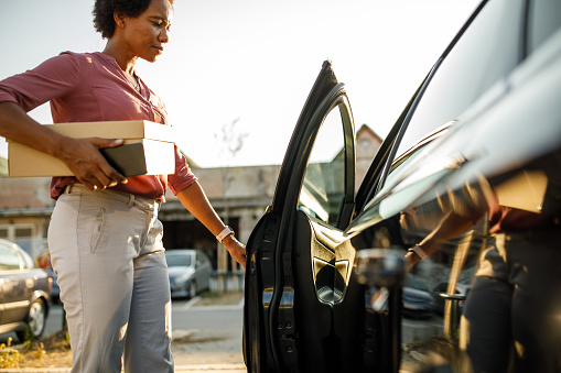 Copy space shot of mid adult woman opening the door on the driver's side of her car after picking a package from the post office.