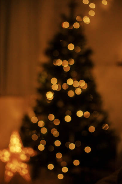 istock Blurry illuminated christmas tree in eve. Abstract blurred christmas tree with golden lights in evening room. Atmospheric christmas image, magic winter time 1424677425